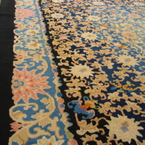 A large navy and beige floral rug with a black outer border rests on light hardwood flooring.
