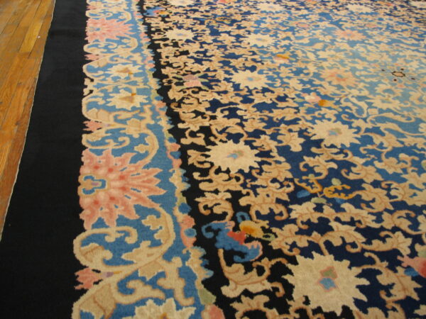 A large navy and beige floral rug with a black outer border rests on light hardwood flooring.