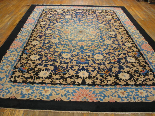 Navy and beige floral rug with pink accents and a shaded blue center displayed on wood planks.