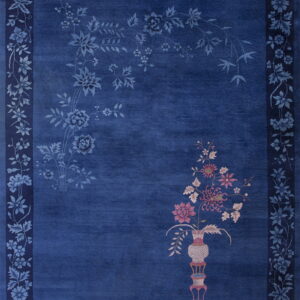 A cobalt blue rug displays tone-on-tone flowers, a floral border, and a pink-accented vase motif.