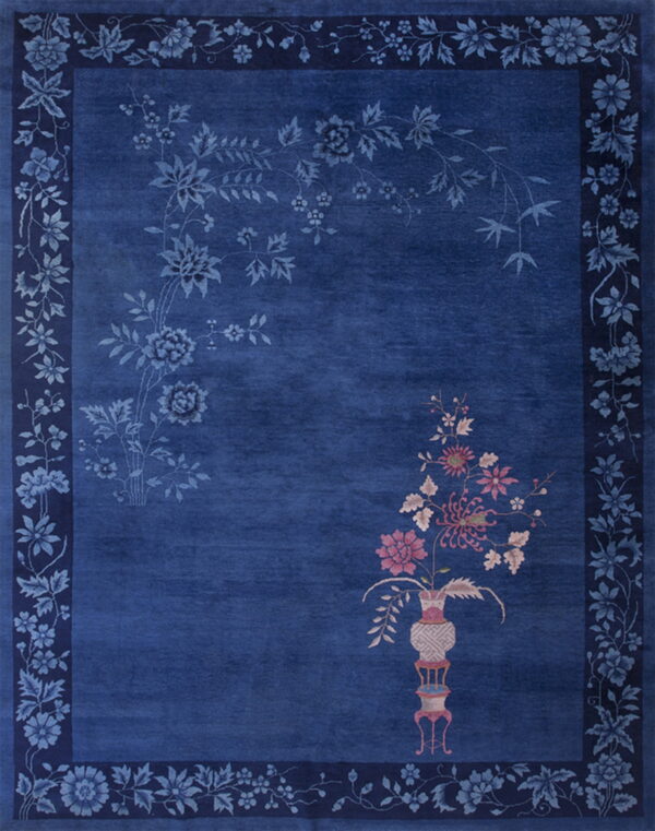 A cobalt blue rug displays tone-on-tone flowers, a floral border, and a pink-accented vase motif.