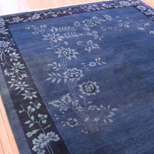Dark indigo rug featuring light blue botanical motifs and a patterned border on light wood planks.