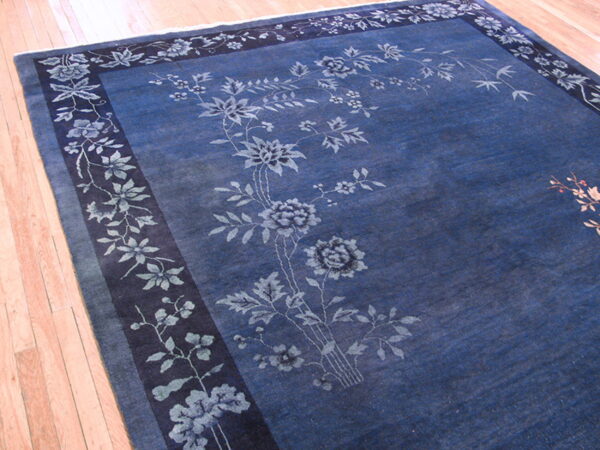 Dark indigo rug featuring light blue botanical motifs and a patterned border on light wood planks.