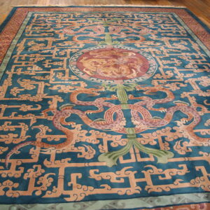 Teal rug featuring central dragon motifs and intricate tan geometric fretwork, displayed on wood plank flooring.