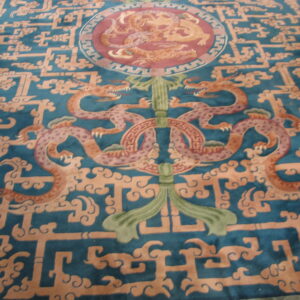 A detailed rug features orange and pink dragons centered on a deep teal background with geometric lattice and cloud patterns.