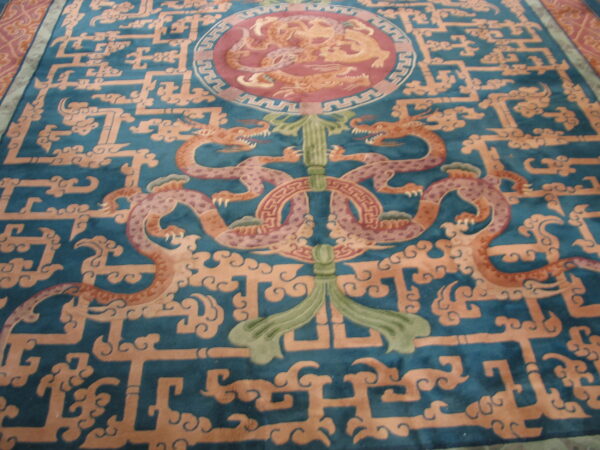 A detailed rug features orange and pink dragons centered on a deep teal background with geometric lattice and cloud patterns.