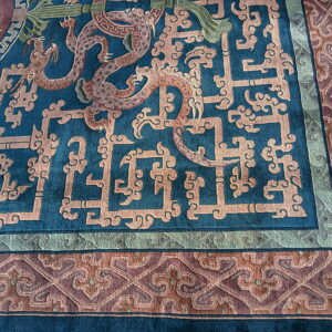Detailed teal rug with peach fretwork and dragon motifs surrounding a complex maroon and green border.