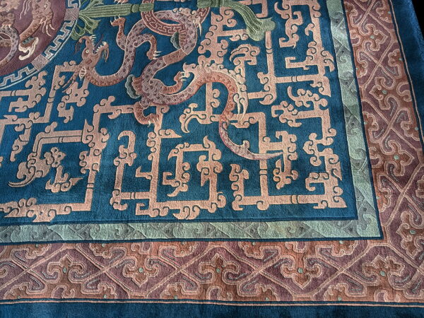 Detailed teal rug with peach fretwork and dragon motifs surrounding a complex maroon and green border.