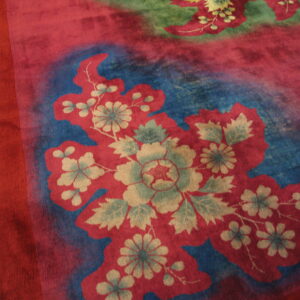 Red, blue, and green high-pile rug with large stylized floral patterns rests on light hardwood flooring.