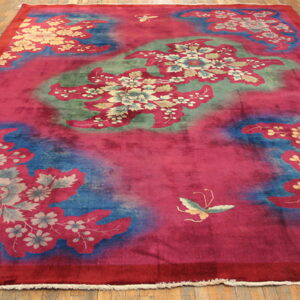 High-pile magenta rug featuring gold and gray floral motifs over mottled blue and green sections on a wood floor.