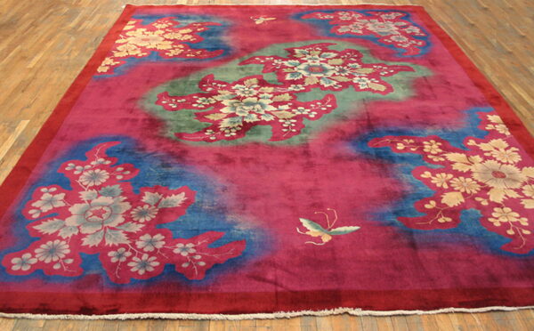 High-pile magenta rug featuring gold and gray floral motifs over mottled blue and green sections on a wood floor.