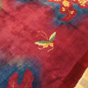 Red plush rug displaying a butterfly and blue botanical patterns rests on light brown wood flooring.