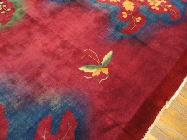 Red plush rug displaying a butterfly and blue botanical patterns rests on light brown wood flooring.