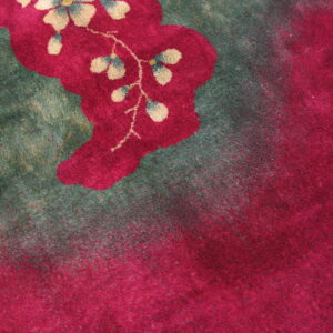 Plush rug detail featuring bright magenta flowers with tan accents bordering a deep green field.