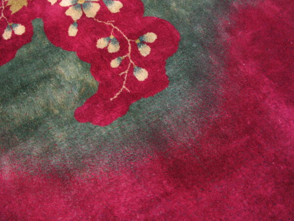 Plush rug detail featuring bright magenta flowers with tan accents bordering a deep green field.