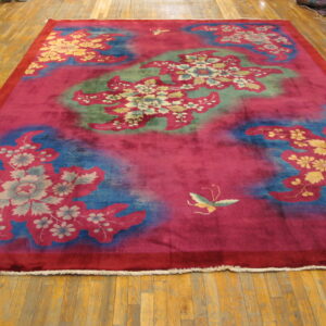 Vibrant magenta rug with large stylized blue and green floral patterns rests on a hardwood floor.