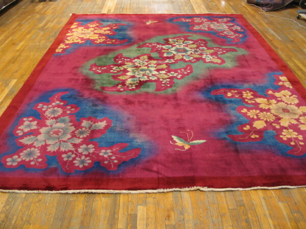Vibrant magenta rug with large stylized blue and green floral patterns rests on a hardwood floor.