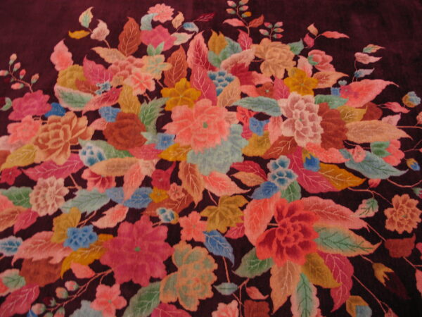 Multicolor floral pattern on a deep burgundy rug, featuring dense pink, green, blue, and gold motifs.