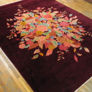 Deep burgundy rug featuring a center multicolored floral spray on light wood plank flooring.