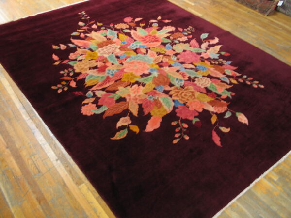 Deep burgundy rug featuring a center multicolored floral spray on light wood plank flooring.