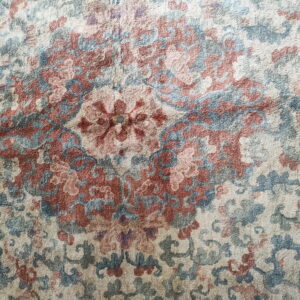 Close view of a traditional rug medallion pattern in cream, dusty blue, and terracotta red pile.