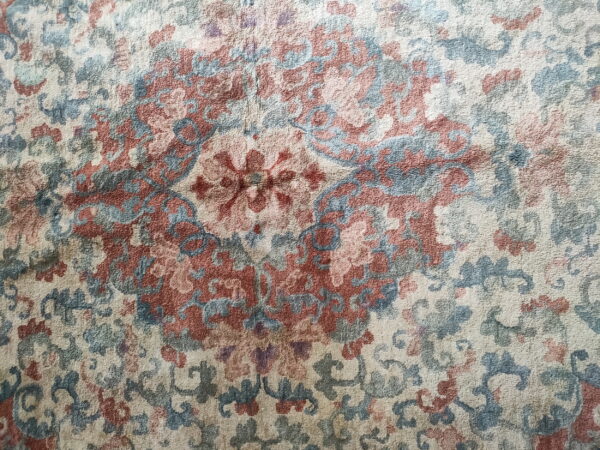 Close view of a traditional rug medallion pattern in cream, dusty blue, and terracotta red pile.