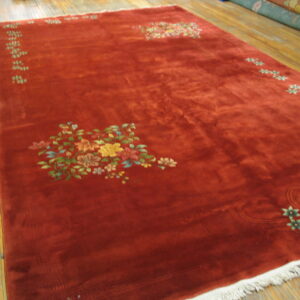 Plush rust-red rug featuring large and small multicolored floral motifs on a light wood floor.