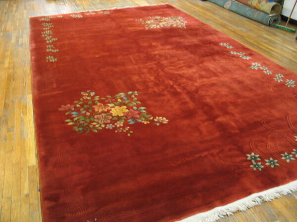 Plush rust-red rug featuring large and small multicolored floral motifs on a light wood floor.