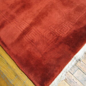 Plush rust rug with carved geometric detail and white fringe on distressed wood floors.