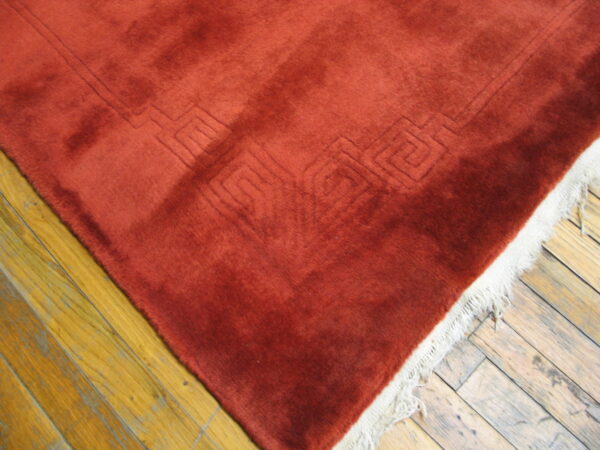 Plush rust rug with carved geometric detail and white fringe on distressed wood floors.