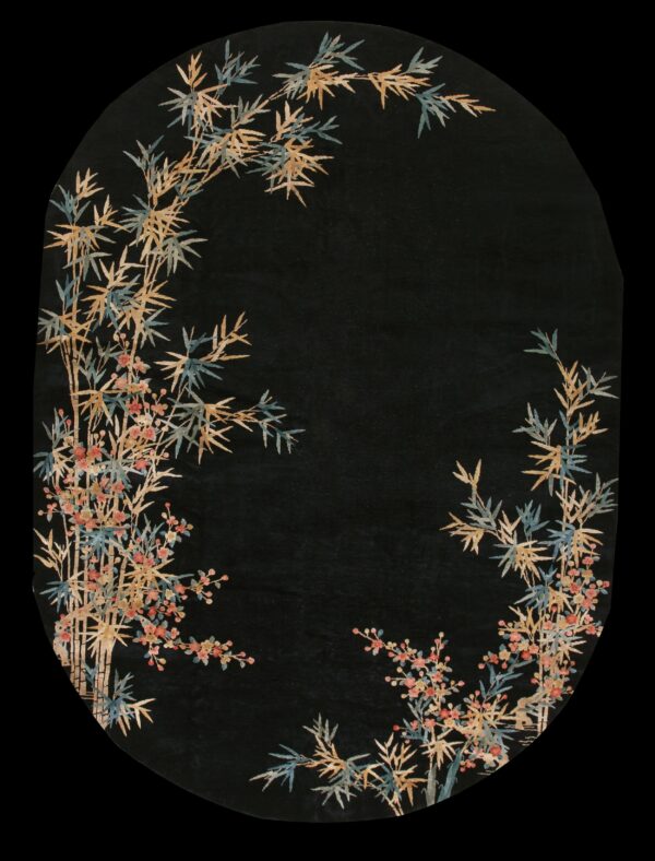 Black oval rug featuring a bamboo and floral border in tan, blue, and pink against a dark field.