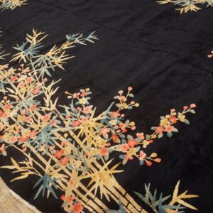 A black rug features a gold bamboo and pink floral design on light wooden flooring.