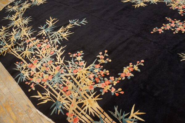 A black rug features a gold bamboo and pink floral design on light wooden flooring.