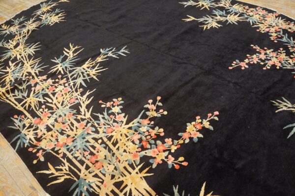 A thick black pile rug detailed with light blue and golden bamboo and pink flowering branches.