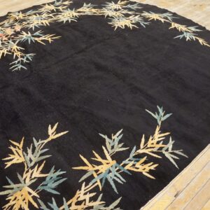 Black oval rug with medium pile, patterned with yellow and teal bamboo leaves on hardwood.
