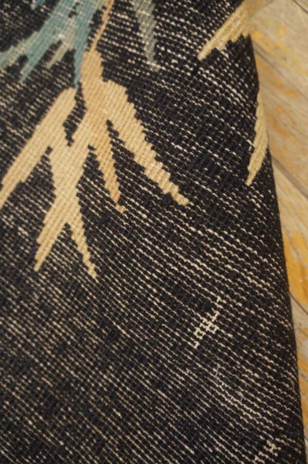 Woven rug detail showing black, tan, and teal geometric patterns on light wooden floor.