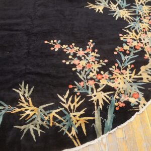 A round black rug with yellow, teal, and pink floral and bamboo patterns rests on wood flooring.