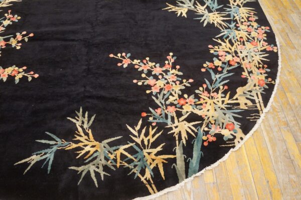 A round black rug with yellow, teal, and pink floral and bamboo patterns rests on wood flooring.