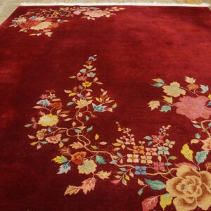 Red rug with a lustrous pile and multicolored floral pattern spreading across a light wood floor.
