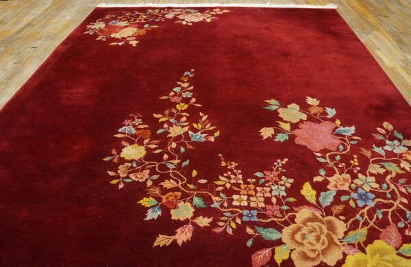 Red rug with a lustrous pile and multicolored floral pattern spreading across a light wood floor.