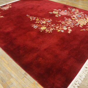 Burgundy area rug with scattered multi-colored floral designs and visible cream fringe on distressed wood flooring.