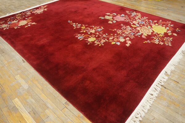 Burgundy area rug with scattered multi-colored floral designs and visible cream fringe on distressed wood flooring.