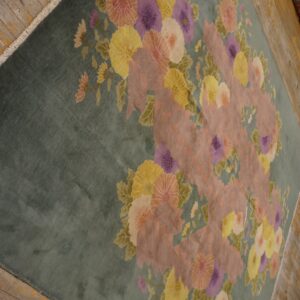 Teal floral rug featuring large pink, purple, and yellow blossoms rests on distressed wood flooring.
