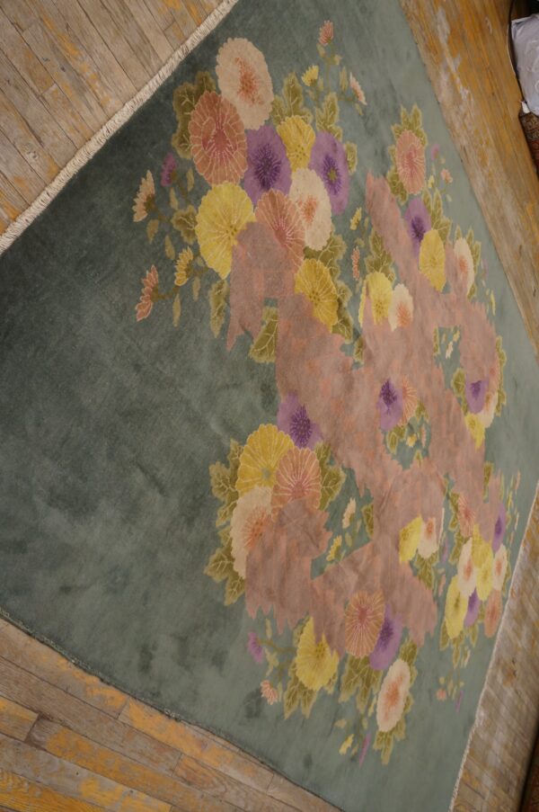 Teal floral rug featuring large pink, purple, and yellow blossoms rests on distressed wood flooring.