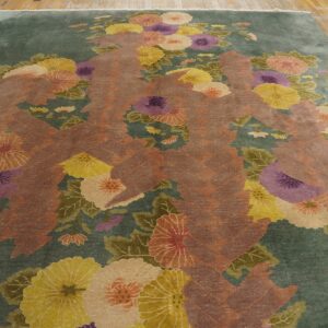 Teal-green rug with pink, yellow, and purple floral patterns surrounding a rust-colored zigzag shape on wood floor.