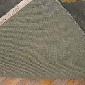 The green, diagonally ribbed backing of a floral rug is visible with fringe on distressed wood flooring.