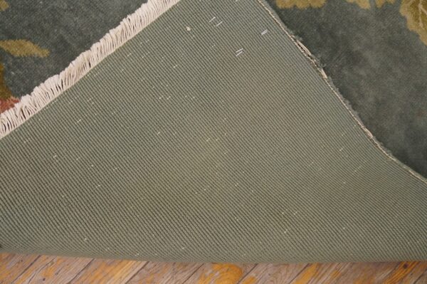 The green, diagonally ribbed backing of a floral rug is visible with fringe on distressed wood flooring.