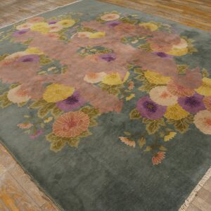 Muted blue-green rug with pink, yellow, and purple floral pattern rests on distressed wood planks.