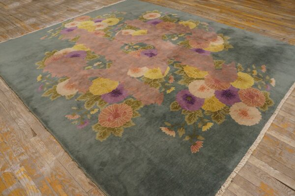 Muted blue-green rug with pink, yellow, and purple floral pattern rests on distressed wood planks.