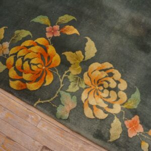 Detail shot of a plush teal rug featuring stylized orange and gold flowers on wood plank flooring.